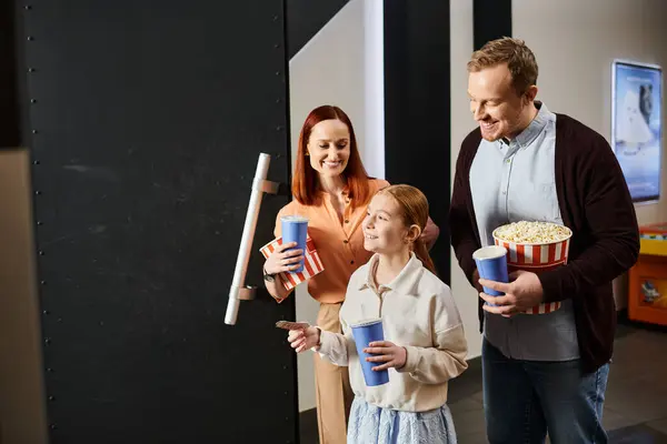 Un uomo, una donna e un bambino che tengono felicemente secchi di popcorn al cinema, godendosi una gita in famiglia. — Foto stock