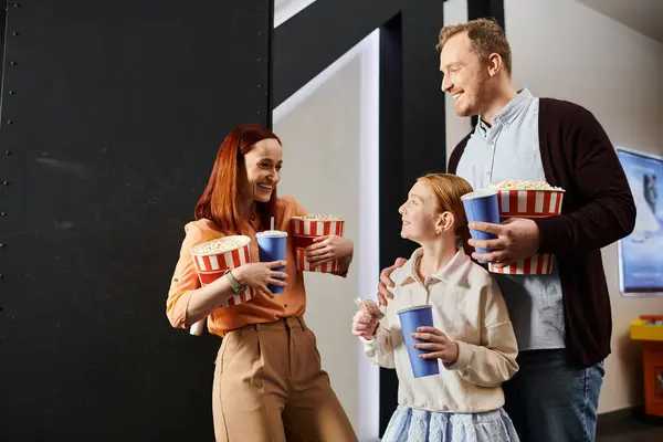 A man, woman, and child happily hold popcorn boxes, spending quality time together at the cinema. — Stock Photo