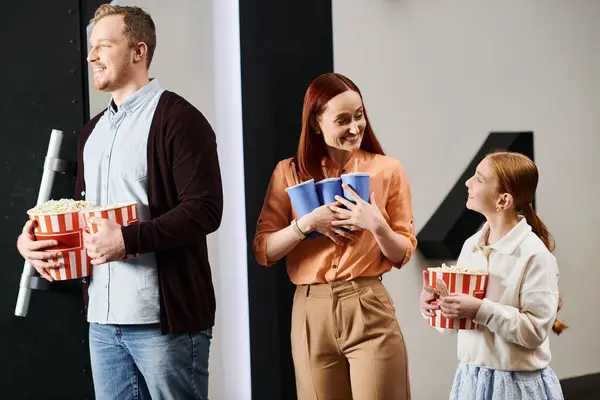 A happy family stands close together, enjoying a movie together at the cinema. — Stock Photo