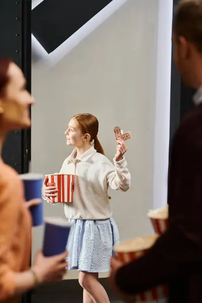Девушка радостно держит коробку с попкорном и билеты, наслаждаясь вечером семейного кино в кинотеатре. — стоковое фото