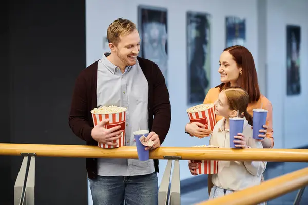 A man and a woman joyfully hold cups of popcorn, enjoying a family movie outing together at the cinema. — Stock Photo
