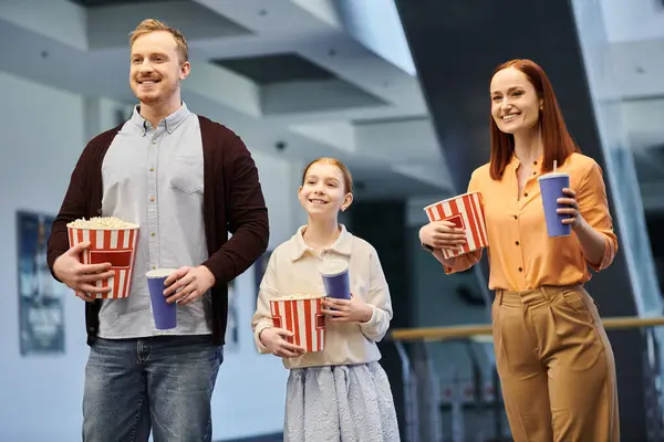 Щаслива сім'я, що складається з чоловіка, жінки та дитини, радісно тримає попкорн, проводячи якісний час разом у кінотеатрі. — стокове фото