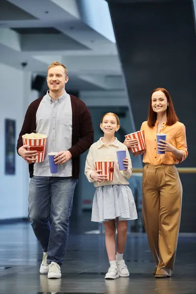 Un homme, une femme et un enfant marchant joyeusement dans une salle de cinéma, profitant de moments de famille de qualité ensemble. — Photo de stock