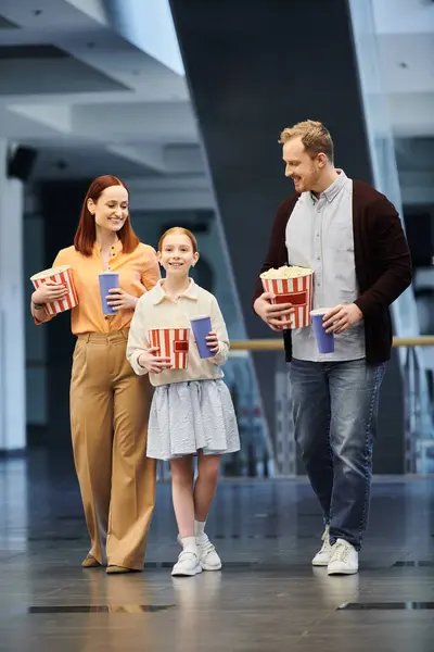 A man, woman, and child joyfully hold popcorn boxes as they spend quality time together at the cinema. — Stock Photo