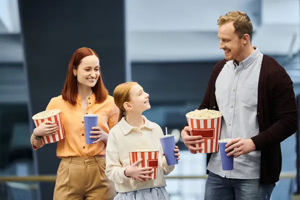A man, woman, and two children happily holding popcorn cups while enjoying a movie night together at the cinema. — Stock Photo
