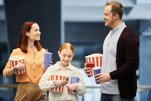 Un hombre, una mujer y un niño felices sosteniendo palomitas de maíz mientras disfrutan de una noche de cine juntos en el cine. - foto de stock