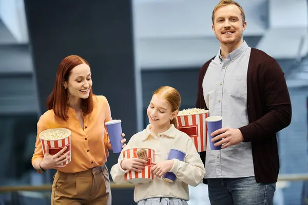 Ein Mann, eine Frau und ein Kind halten fröhlich Popcorndosen in der Hand, während sie einen Kinoabend genießen. — Stockfoto