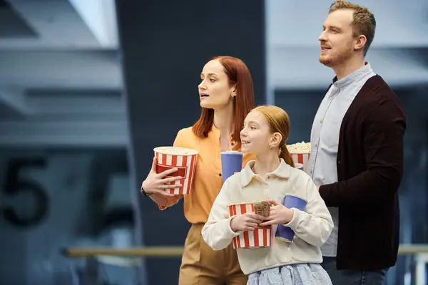 Un uomo e la sua famiglia tengono gioiosamente tazze di popcorn, godendo di una gita in famiglia al cinema. — Foto stock