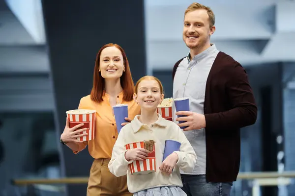 Ein Mann, eine Frau und ein Kind halten fröhlich Popcorndosen in einem Kino und genießen die gemeinsame Zeit. — Stockfoto