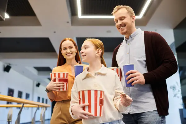 A happy family stands side by side, each holding a cup, bonding and spending quality time together in a cinema. — Stock Photo