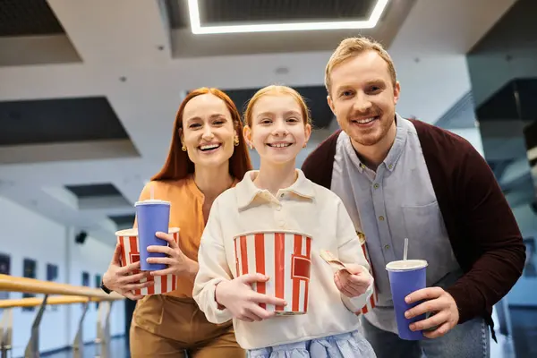 Семья улыбается, держа чашки попкорна, сближаясь и наслаждаясь весело провести время кино вместе в кино. — стоковое фото