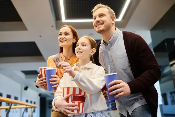 Счастливая семья стоит вместе, держа чашки, наслаждаясь своим временем в кино. — стоковое фото