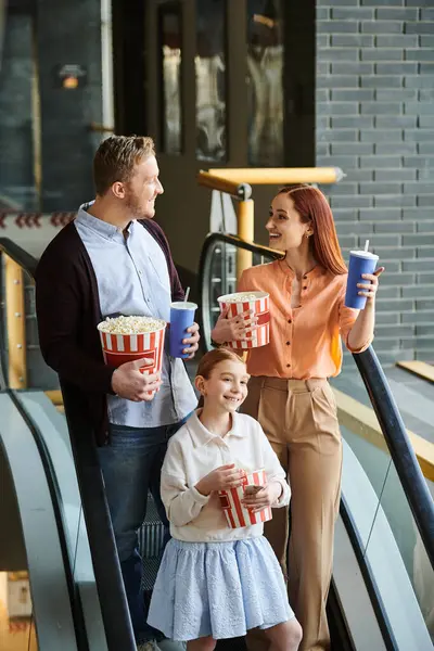 Une famille joyeuse de trois personnes se tient joyeusement sur un escalier roulant dans un cinéma, profitant de leur temps ensemble. — Photo de stock