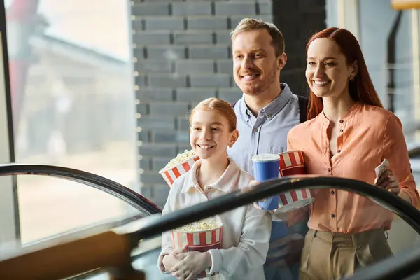 Una famiglia felice di uomini, donne e bambini è in piedi su una scala mobile, sorridendo mentre salgono insieme in un cinema. — Foto stock