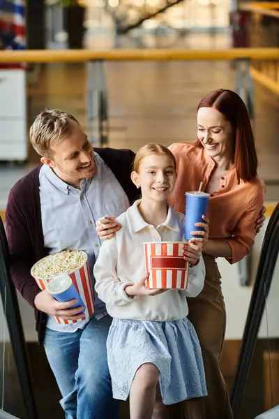 A happy family, clutching popcorn and drinks, sits on an escalator, enjoying a cinema outing together. — Stock Photo