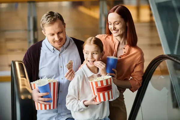 Un uomo, una donna e un bambino mangiano felicemente popcorn insieme al cinema. — Foto stock