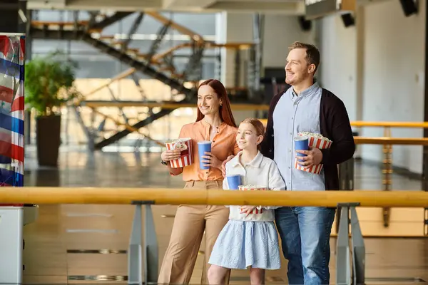 A man, woman, and a child happily hold cups and popcorn, enjoying a moment together in a cinema. — Stock Photo