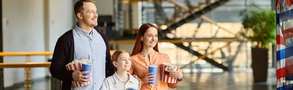 A man, woman, and child happily hold popcorn while watching a film in a cinema. — Stock Photo