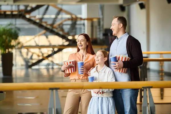 A happy family stands close, each holding a cup as they enjoy a movie together in the cinema. — Stock Photo