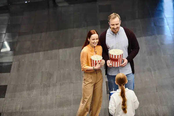 A happy family at the cinema, holding a bucket of popcorn and enjoying a movie together. — Stock Photo
