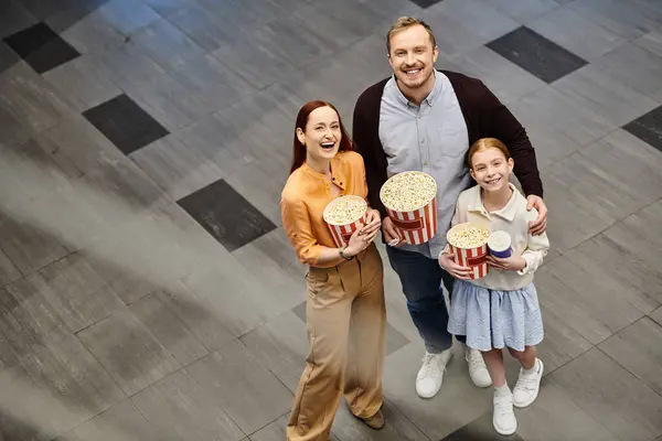 A man and his family happily hold popcorn boxes at the cinema, enjoying a family movie night together. — Stock Photo