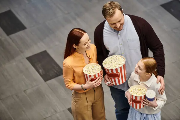 A man and his wife joyfully hold popcorn boxes with kid as they enjoy a movie together at the cinema. — Stock Photo