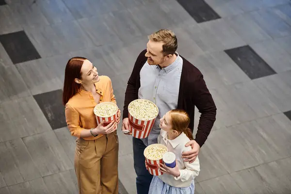 A man and woman excitedly hold popcorn buckets while a child smiles, creating a happy family scene at the cinema. — Stock Photo