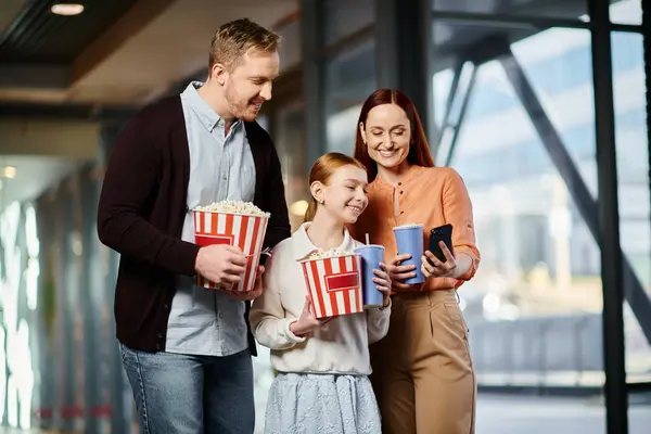 Um homem, mulher e criança alegremente seguram caixas de pipoca enquanto desfrutam de um filme juntos no cinema. — Fotografia de Stock