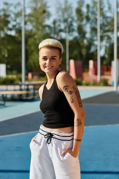 Una joven con el pelo corto se para en una cancha de tenis, mostrando un tatuaje en su brazo. - foto de stock