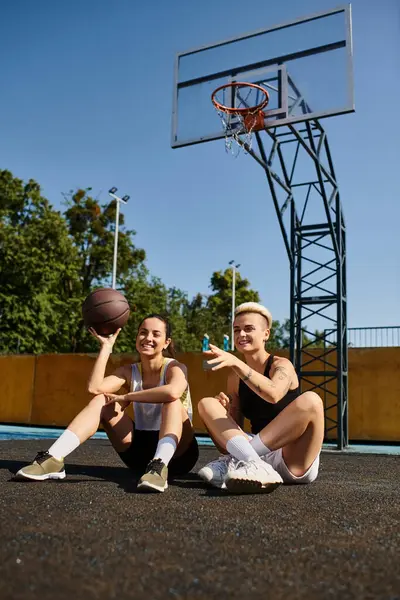 Dos mujeres jóvenes disfrutan de un juego de baloncesto en el suelo bajo el sol de verano. - foto de stock