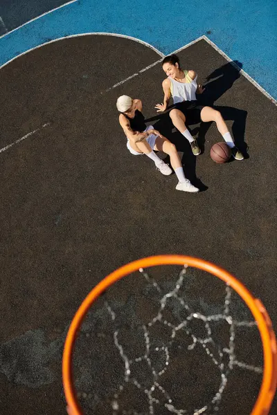Dos jóvenes se levantan triunfalmente sobre una cancha de baloncesto, celebrando su victoria con sonrisas en un soleado día de verano. - foto de stock