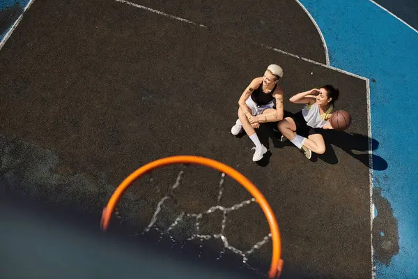 Dos mujeres jóvenes disfrutan de un juego de baloncesto en una soleada cancha al aire libre. - foto de stock