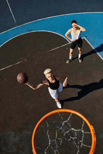 Two athletic women in action on a basketball court, dribbling, shooting, and competing in a thrilling game under the bright sun. — Stock Photo