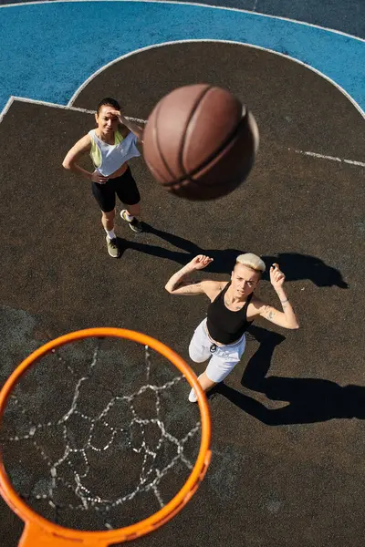 Две молодые женщины, друзья, играют в баскетбол на площадке, демонстрируют свои спортивные способности в летней игре в баскетбол. — стоковое фото