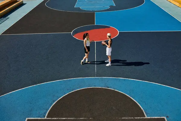 Las mujeres jóvenes hábilmente juegan al baloncesto en una cancha al aire libre, mostrando su atletismo y amistad en el verano. - foto de stock