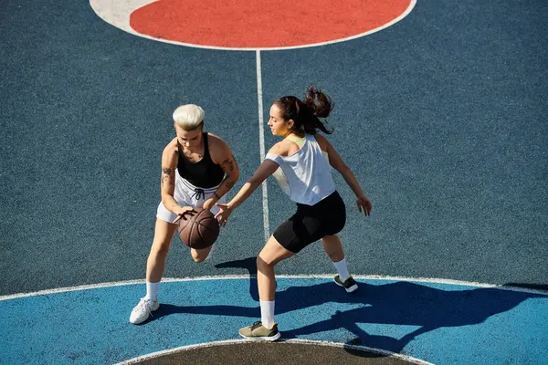 Dos mujeres atléticas están de pie con confianza en una cancha de baloncesto, listas para asumir cualquier desafío que se les presente. - foto de stock