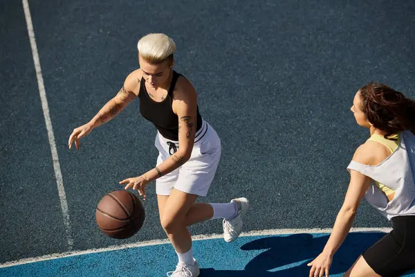 Напряженная игра в баскетбол между двумя молодыми женщинами, друзьями, демонстрирующими свои спортивные навыки на открытой площадке летом. — стоковое фото