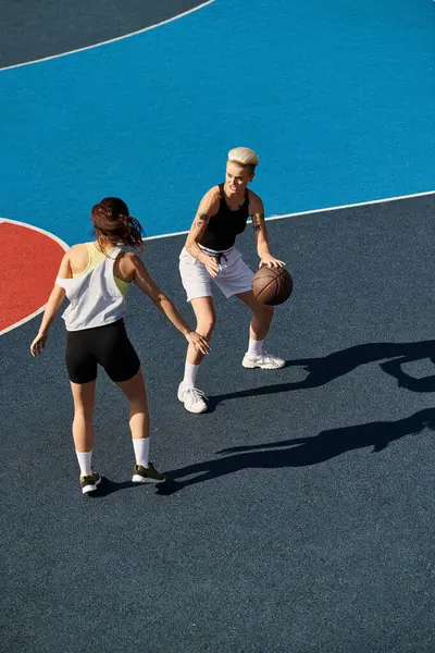 Dos mujeres jóvenes están de pie con confianza en el pico de una cancha de baloncesto, encarnando la fuerza y el trabajo en equipo bajo el sol de verano. - foto de stock