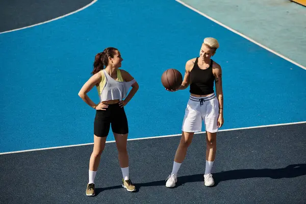 Dos jóvenes atléticas, amigas, se paran con confianza en la parte superior de una cancha de baloncesto, disfrutando de un día de verano.. - foto de stock