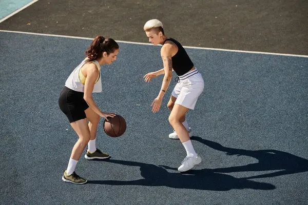 Dos mujeres jóvenes atléticas jugando baloncesto en una cancha al aire libre en el verano. - foto de stock