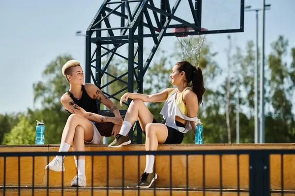 Two young women, athletic and vibrant, engage in conversation on a bench in a sunny outdoor setting, immersed in a moment of bonding and laughter. — Stock Photo