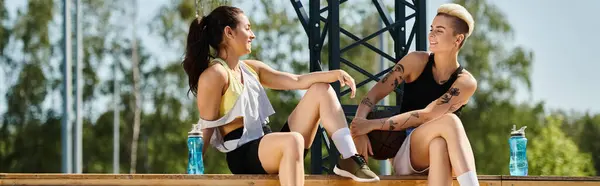 Duas jovens mulheres, amigos, compartilham um momento de camaradagem enquanto se sentam ao lado um do outro em um campo de basquete ao ar livre. — Fotografia de Stock