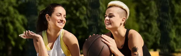 Deux jeunes femmes, amies et athlètes, debout à l'extérieur tenant un ballon de basket-ball, mettant en valeur leur amour pour le sport. — Photo de stock