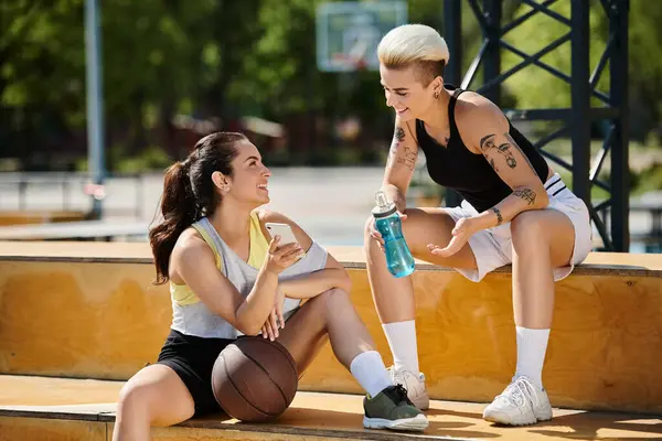Two young women, friends, engaged in a game of basketball outdoors on a sunny day, showcasing their athleticism and teamwork. — Stock Photo