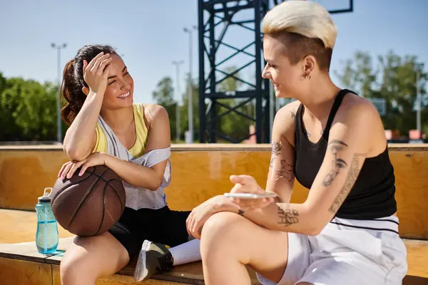 Mujeres jóvenes disfrutando de un partido de baloncesto en un banco bajo el sol de verano. - foto de stock