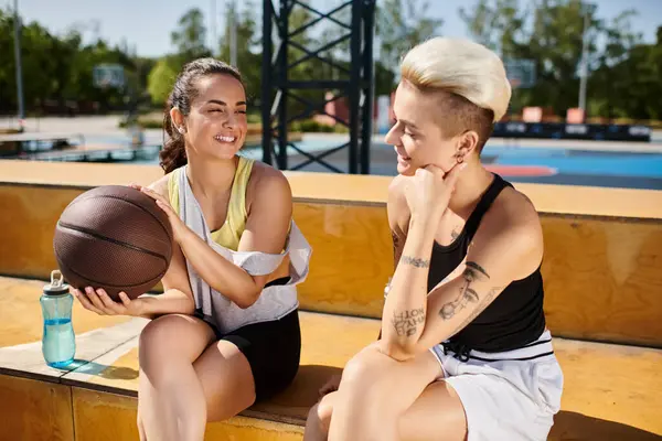 Two athletic women sitting side by side, holding a basketball, enjoying a summer day outdoors. — Stock Photo