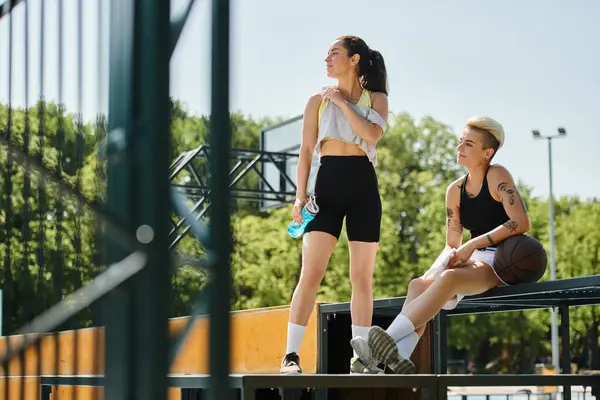 Mujeres jóvenes atléticas tomando un descanso de jugar baloncesto, sentado en la parte superior de un banco bajo el sol de verano. - foto de stock