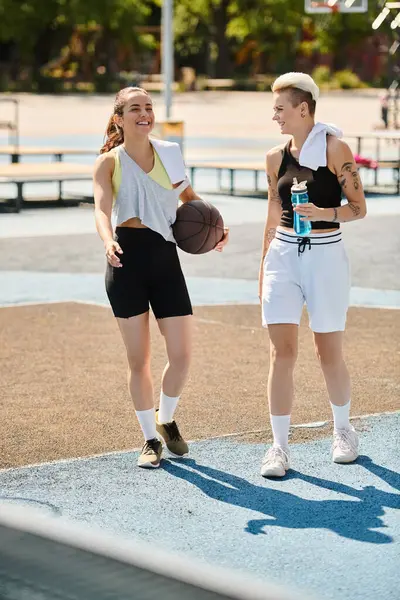 Dos mujeres jóvenes goteando un baloncesto al aire libre, mostrando su atletismo y trabajo en equipo en un día soleado de verano. - foto de stock