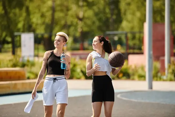 Две атлетичные девушки, друзья, стоят бок о бок на открытом воздухе, держа баскетбольные мячи, готовые к игре. — стоковое фото