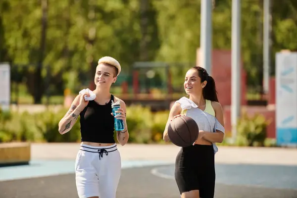 Дві спортивні молоді жінки впевнено стоять на баскетбольному майданчику в сонячний день, втілюючи силу і дружбу. — стокове фото